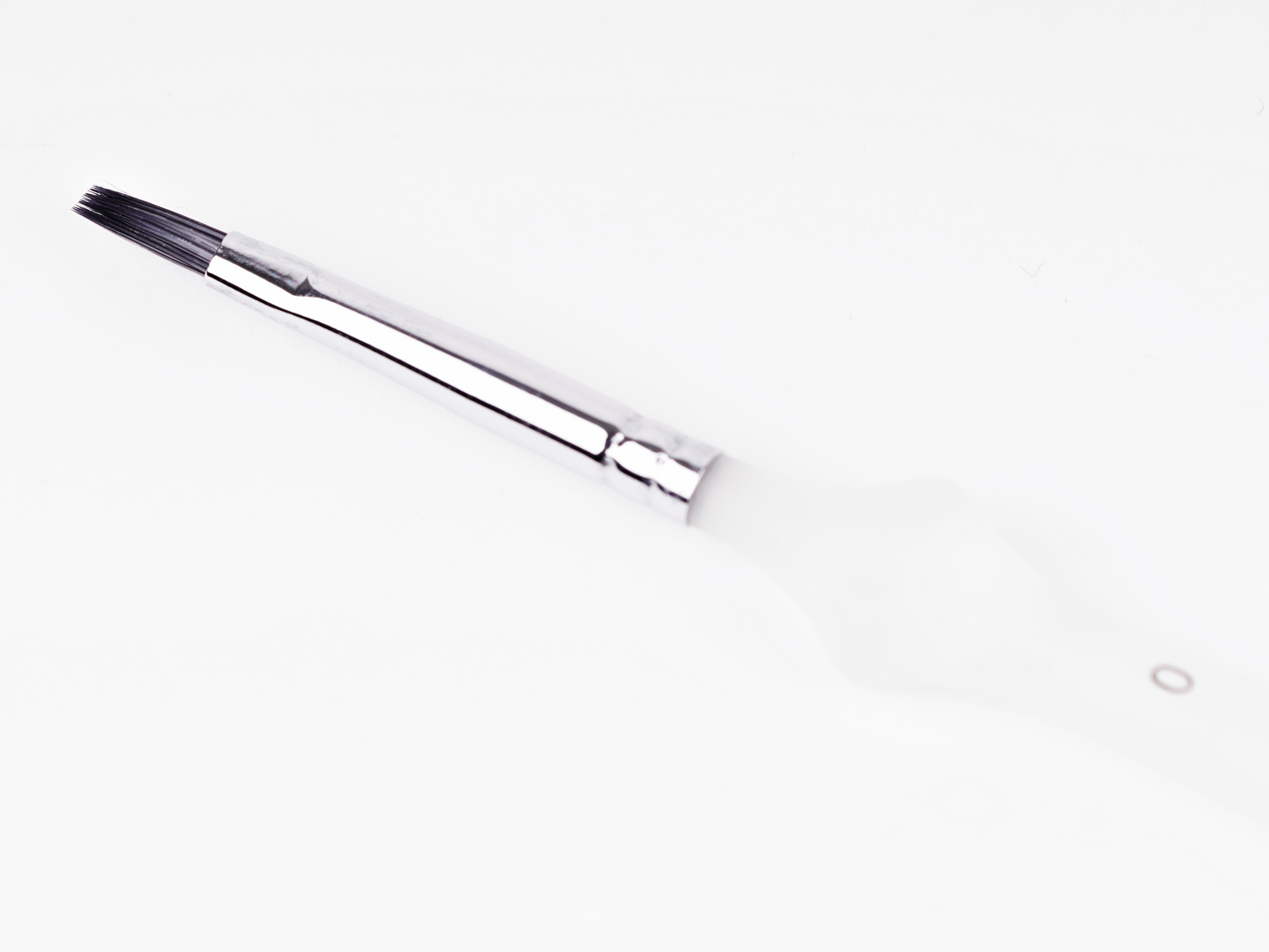 Makeup brush with dark bristles and silver ferrule, angled view