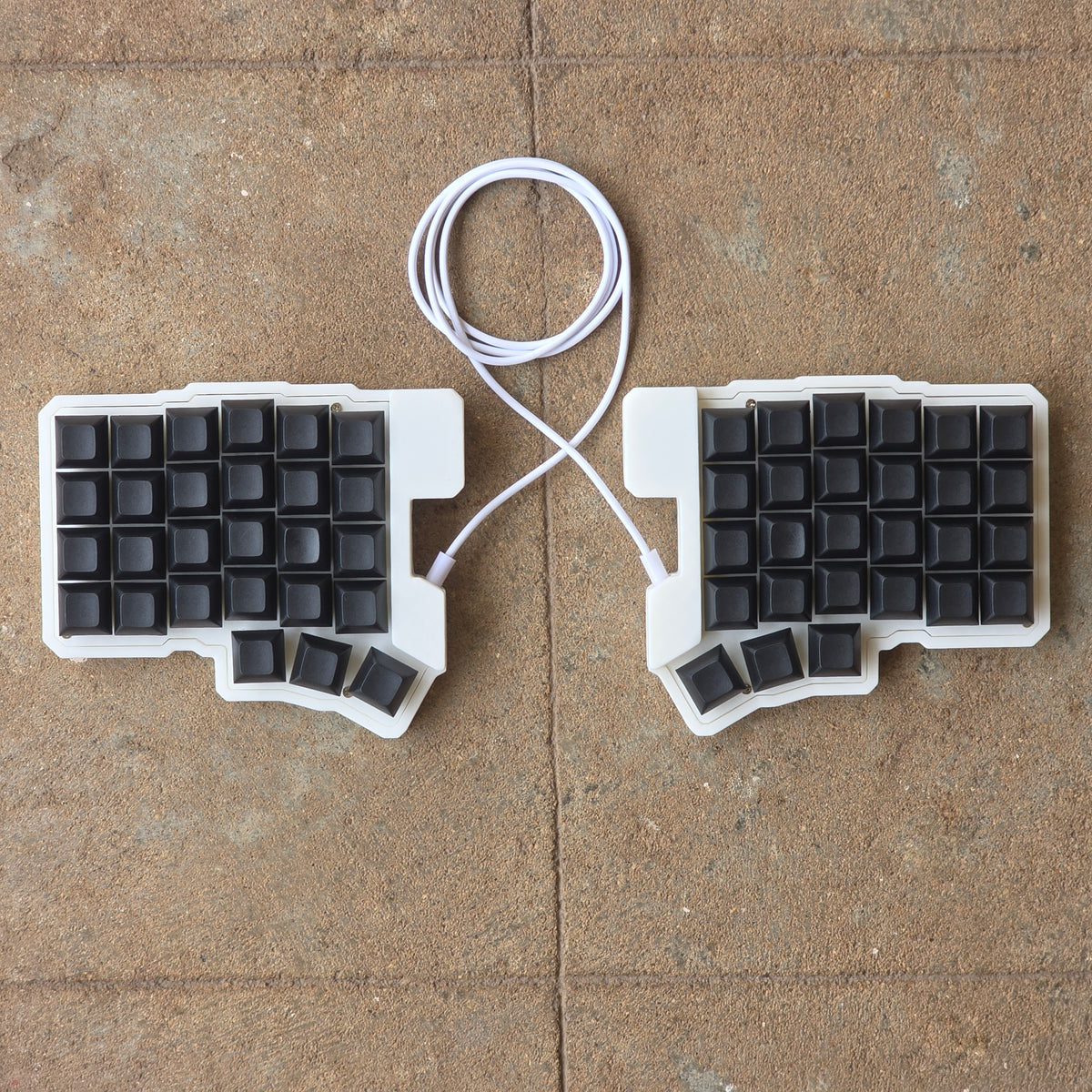 Split wired keyboard with black keycaps and white cable, two-piece layout