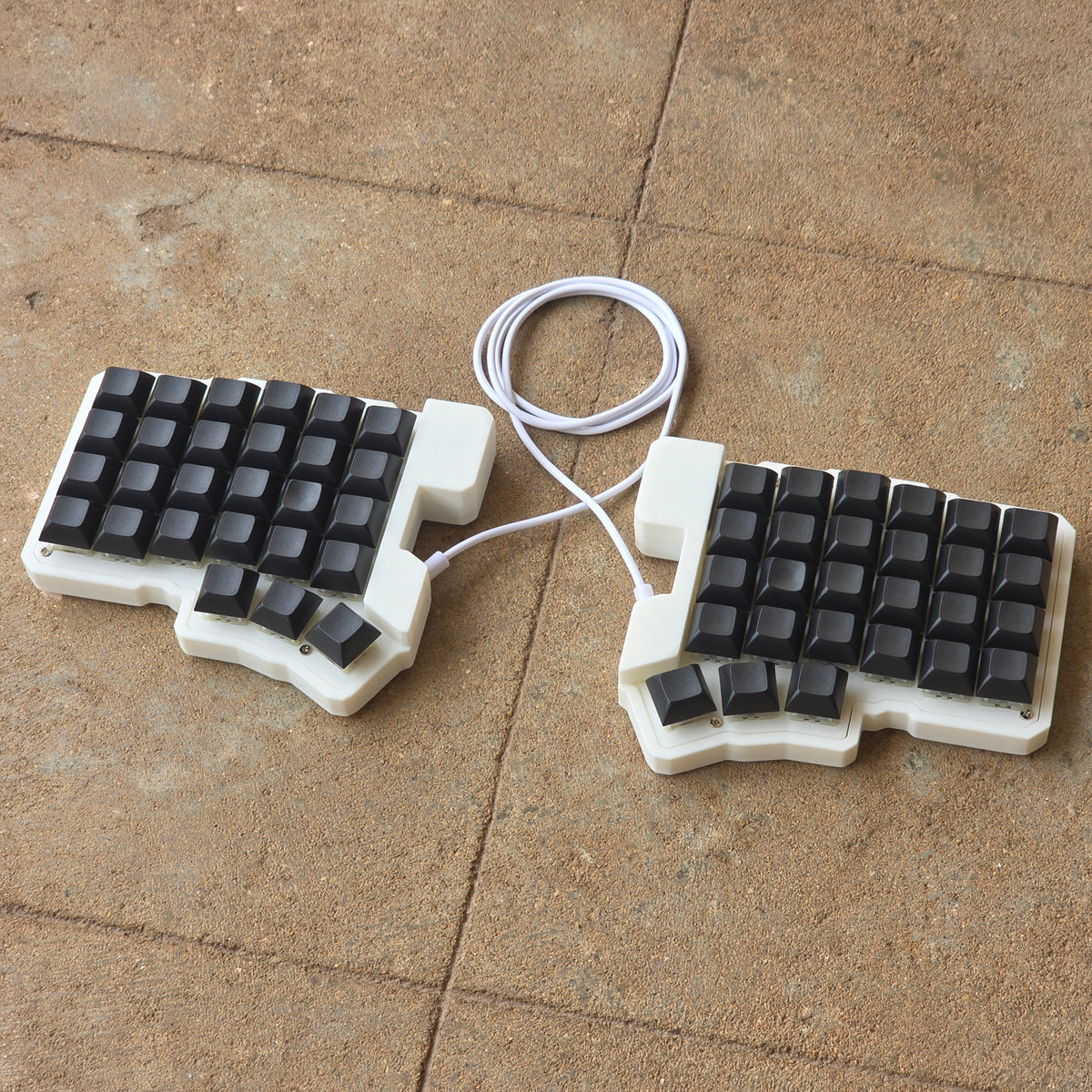 Split wired keyboard with dark keycaps, light base, white cable, angled pair.