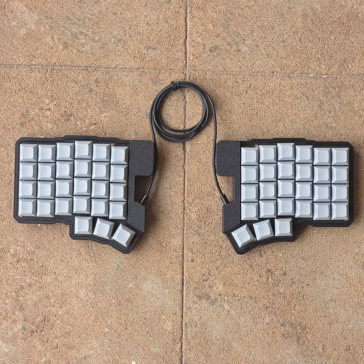 Split wired keyboard with light keycaps, dark base, black cable, top-down pair.