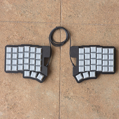 Split wired keyboard with light keycaps, dark base, black cable, top-down pair.