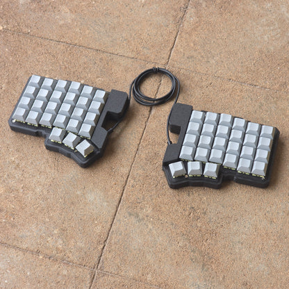 Split wired keyboard with light keycaps, dark base, black cable, angled top view.