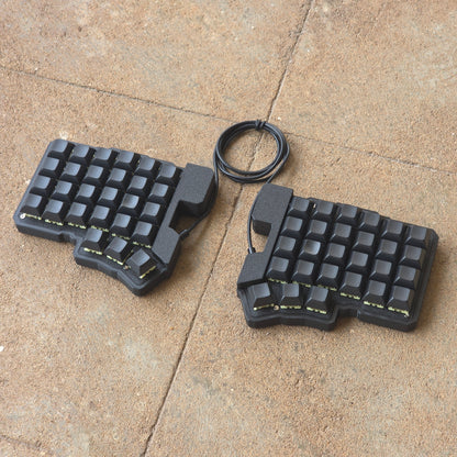 Split wired keyboard with dark keycaps, black base, black cable, angled pair.