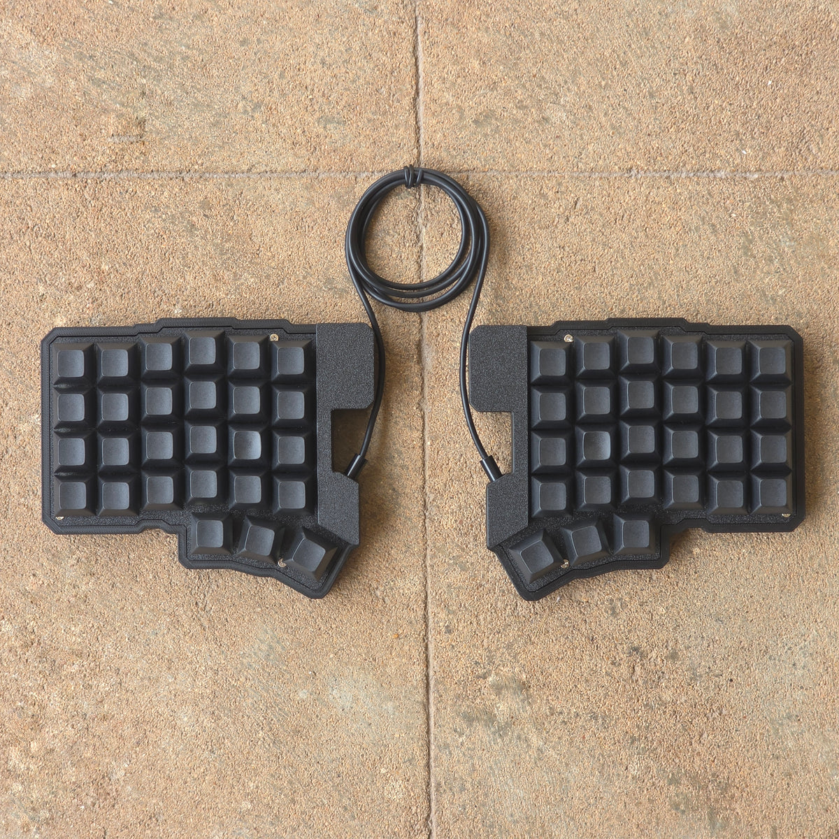 Split wired keyboard with dark keycaps, black base, black cable, front view pair.