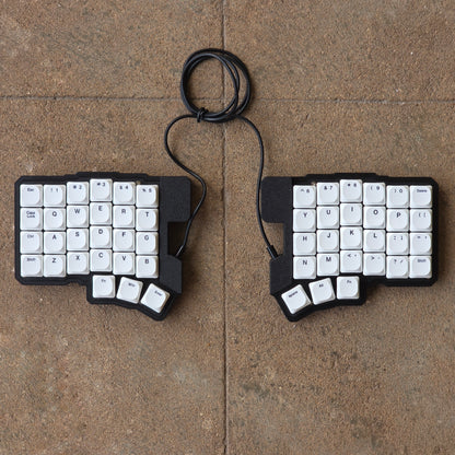 Split wired keyboard with white keycaps and black cable, two-piece layout
