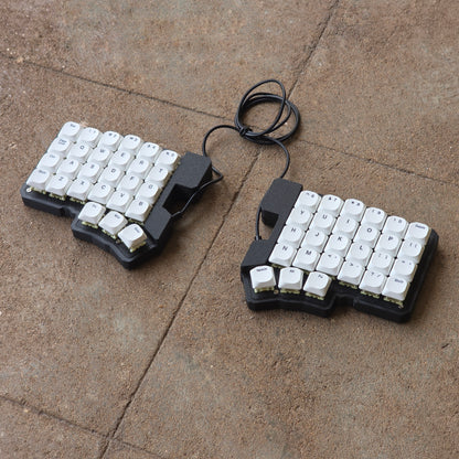 Split wired keyboard with white keycaps and black cable, two-piece layout