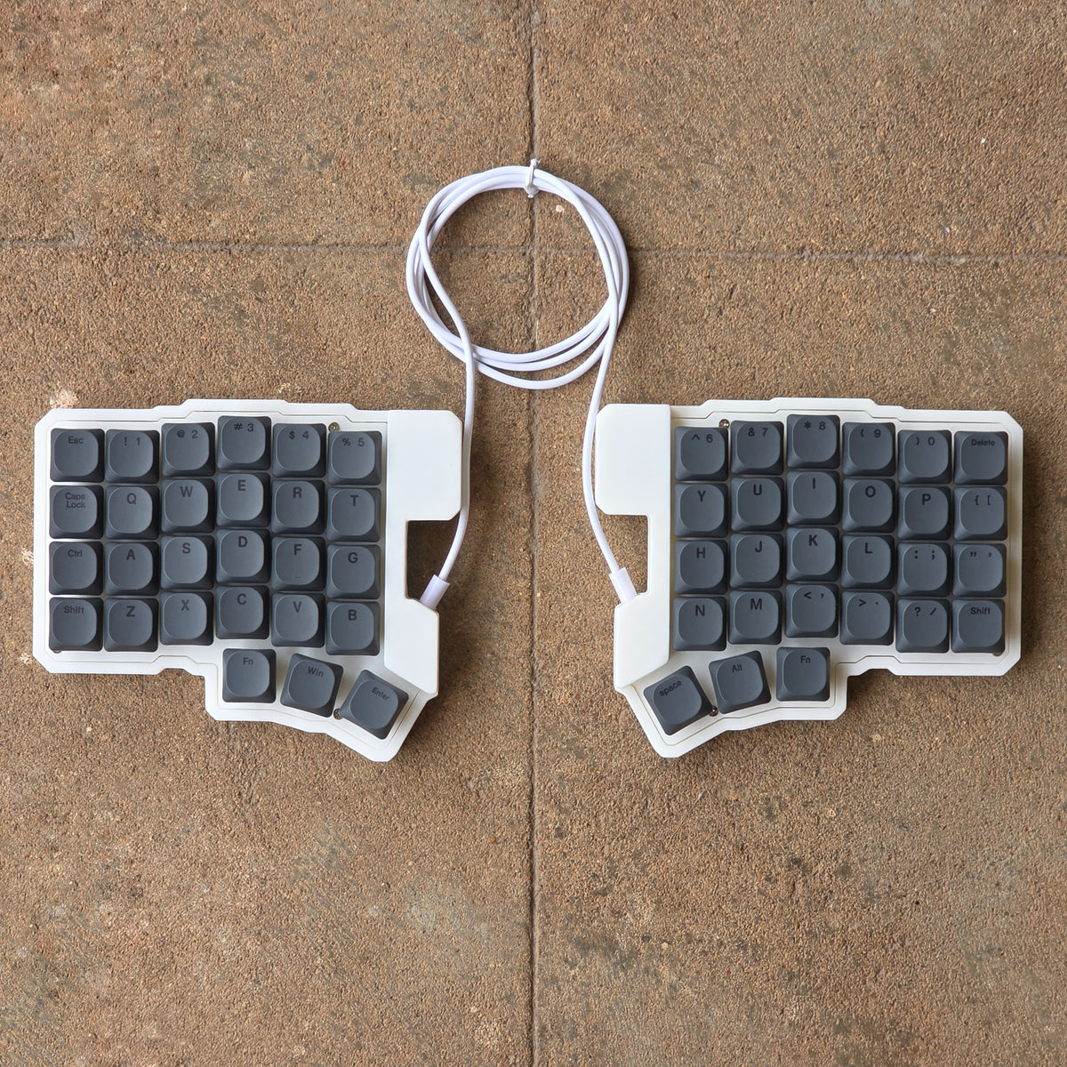 Split wired keyboard with dark gray keycaps and white cable, two-piece layout