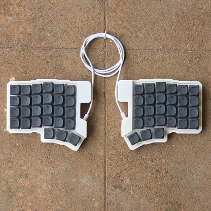Split wired keyboard with dark gray keycaps and white cable, two-piece layout