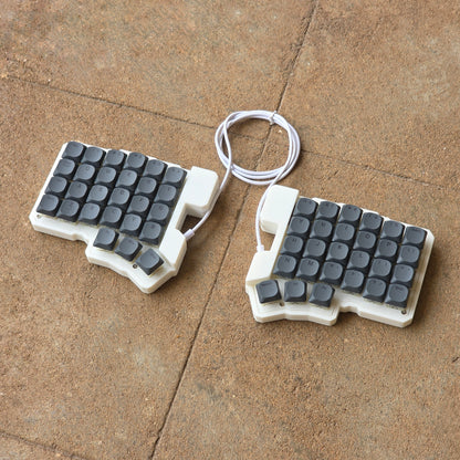 Split wired keyboard with dark gray keycaps and white cable, two-piece layout
