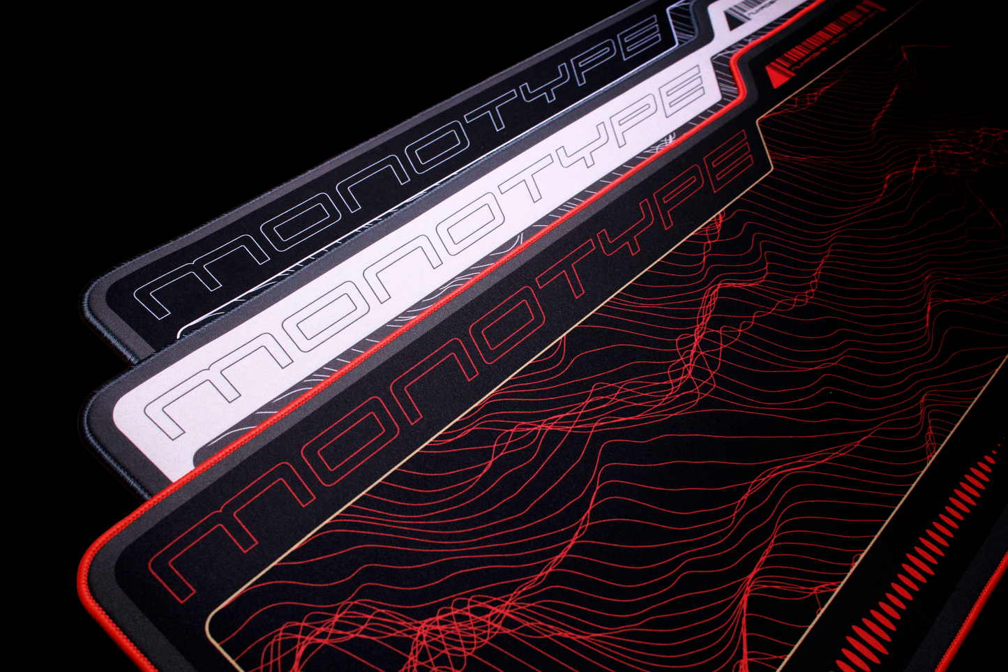 Dark desk mat close-up with red topographic pattern, logo stripe, and red edge trim