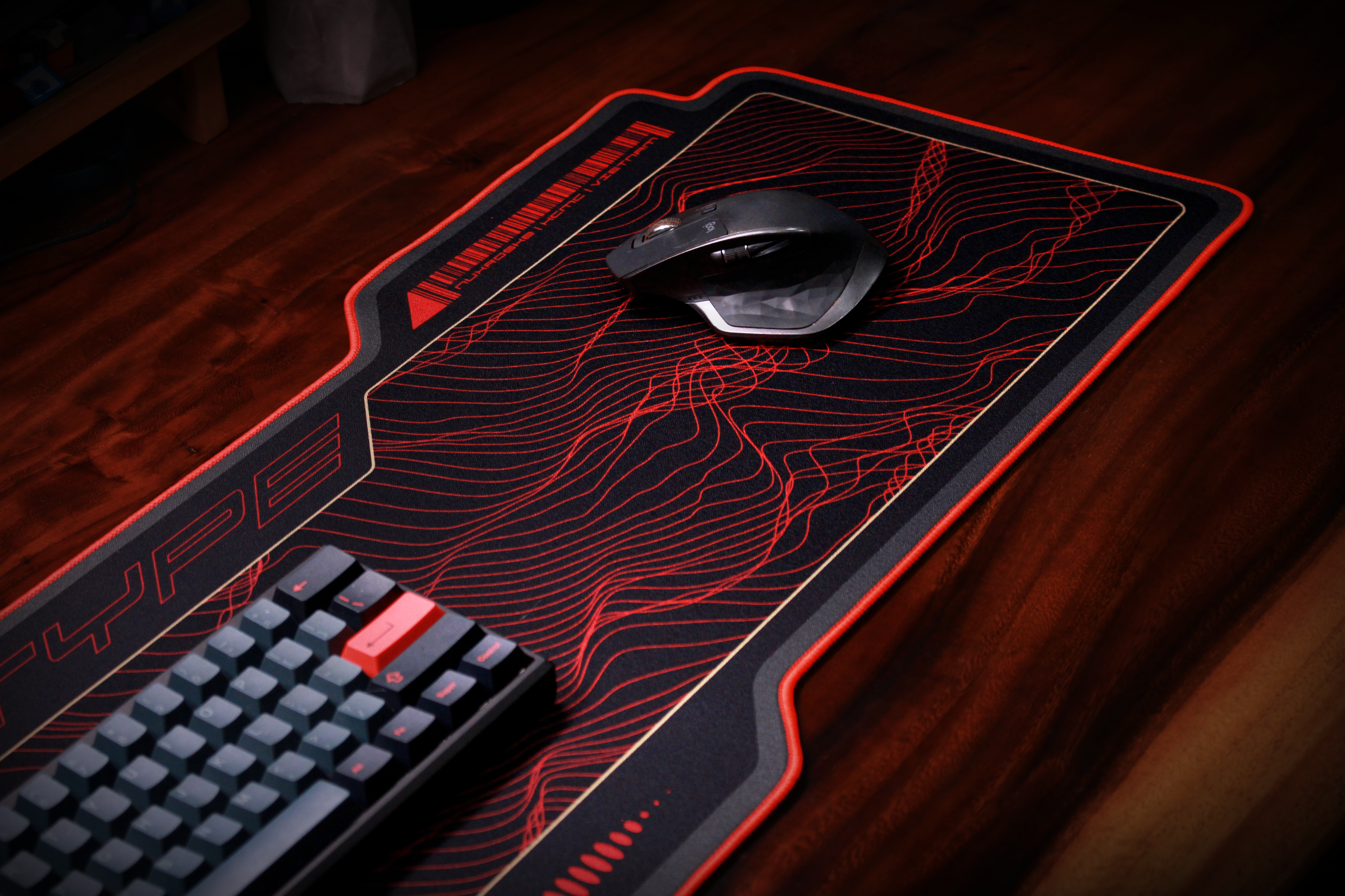 Monotype desk mat, dark gray with red circuit-style line pattern and stitched border