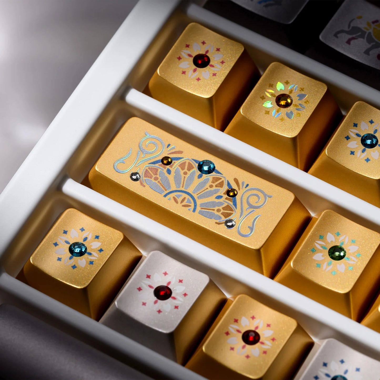 Gold keyboard keycaps with blue and green gem-like designs in a white compartment tray