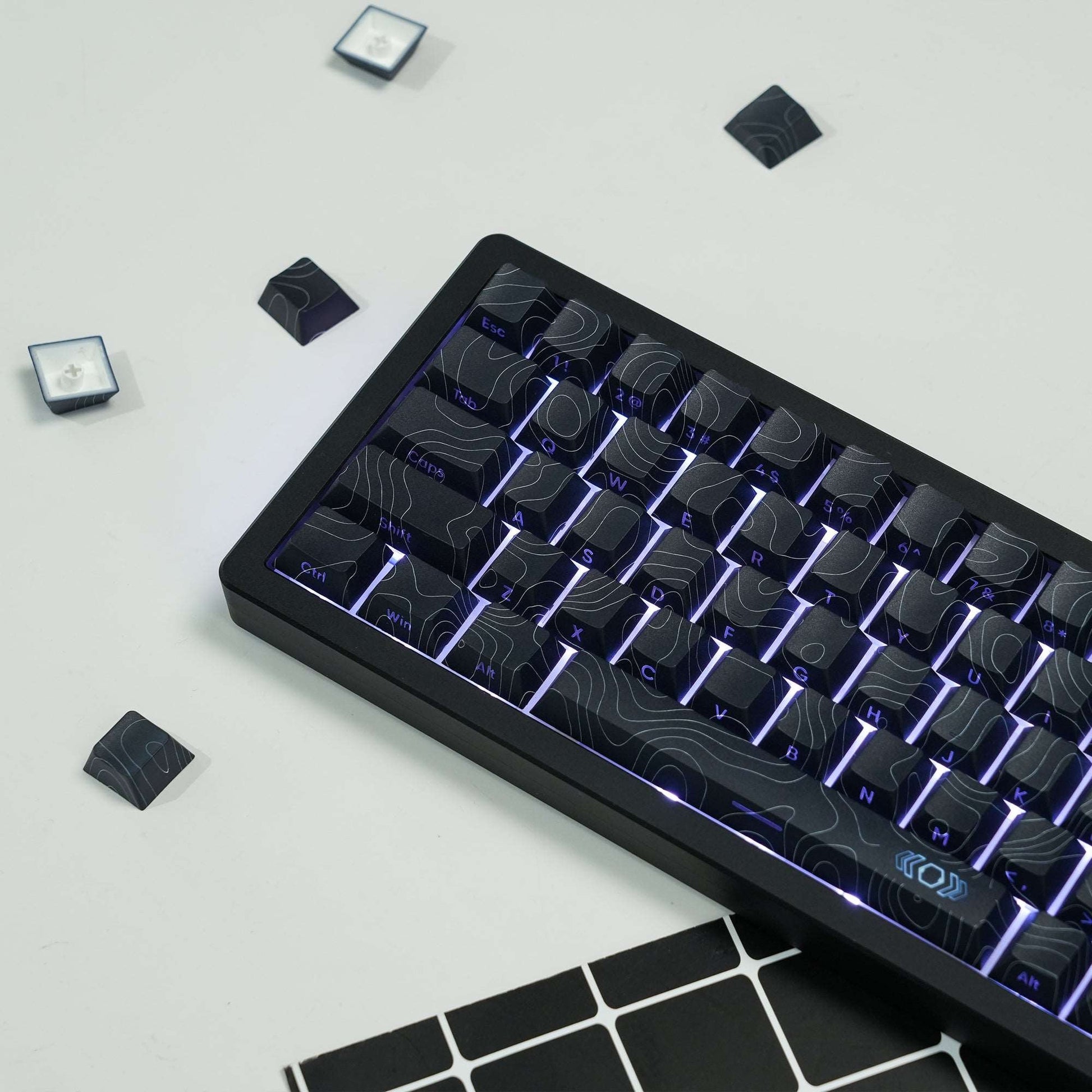 Black topographic keycap set in a dark case, with purple-blue rim lighting