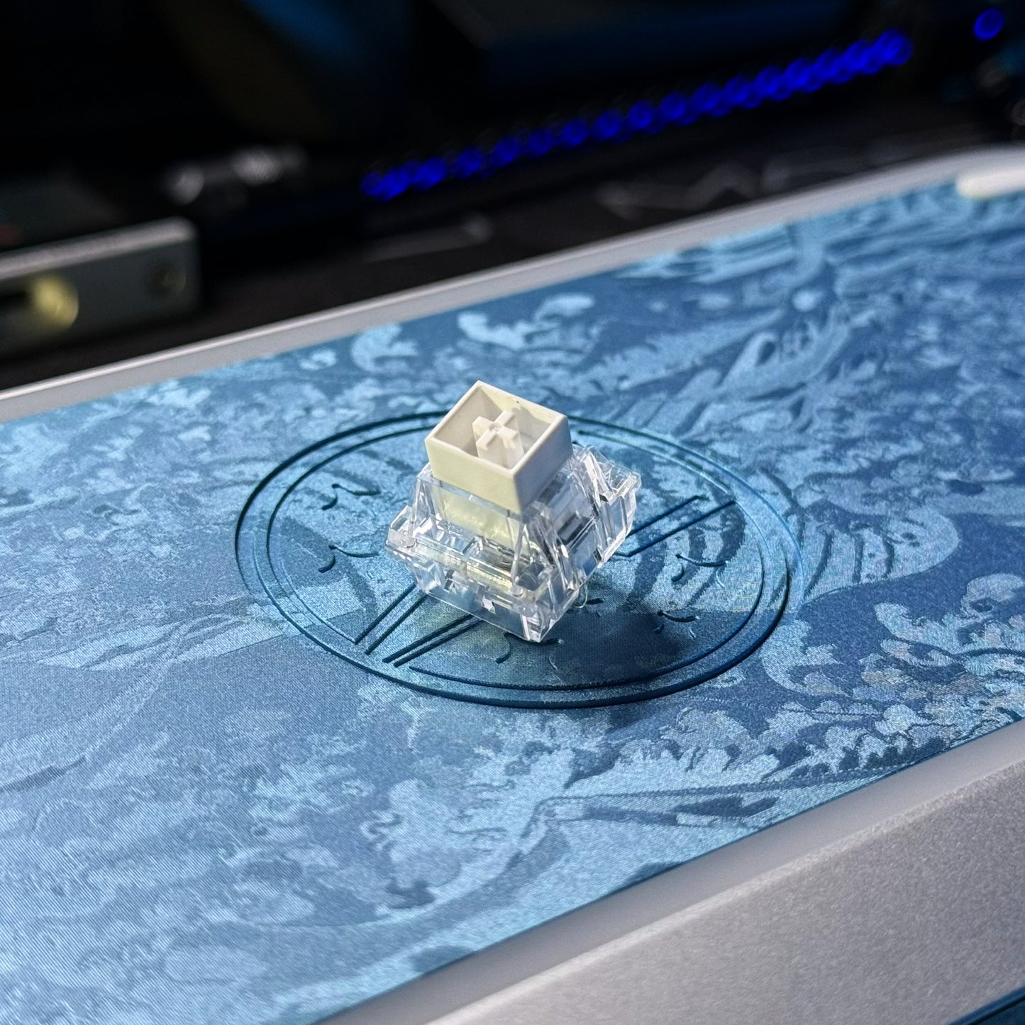 Hall-effect keyboard switch mounted on blue textured surface, clear housing